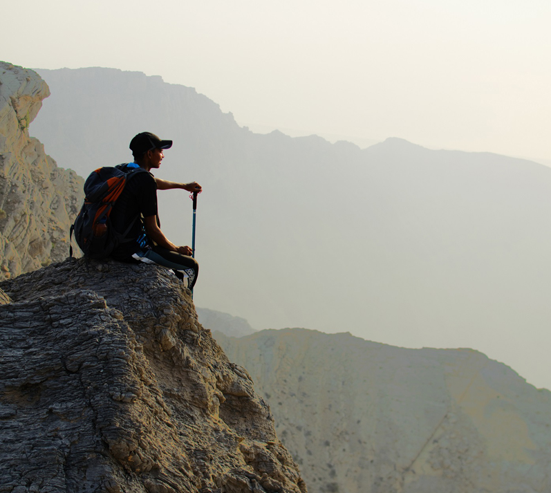 Hiker with a backpack resting on a rocky ledge overlooking the mountains